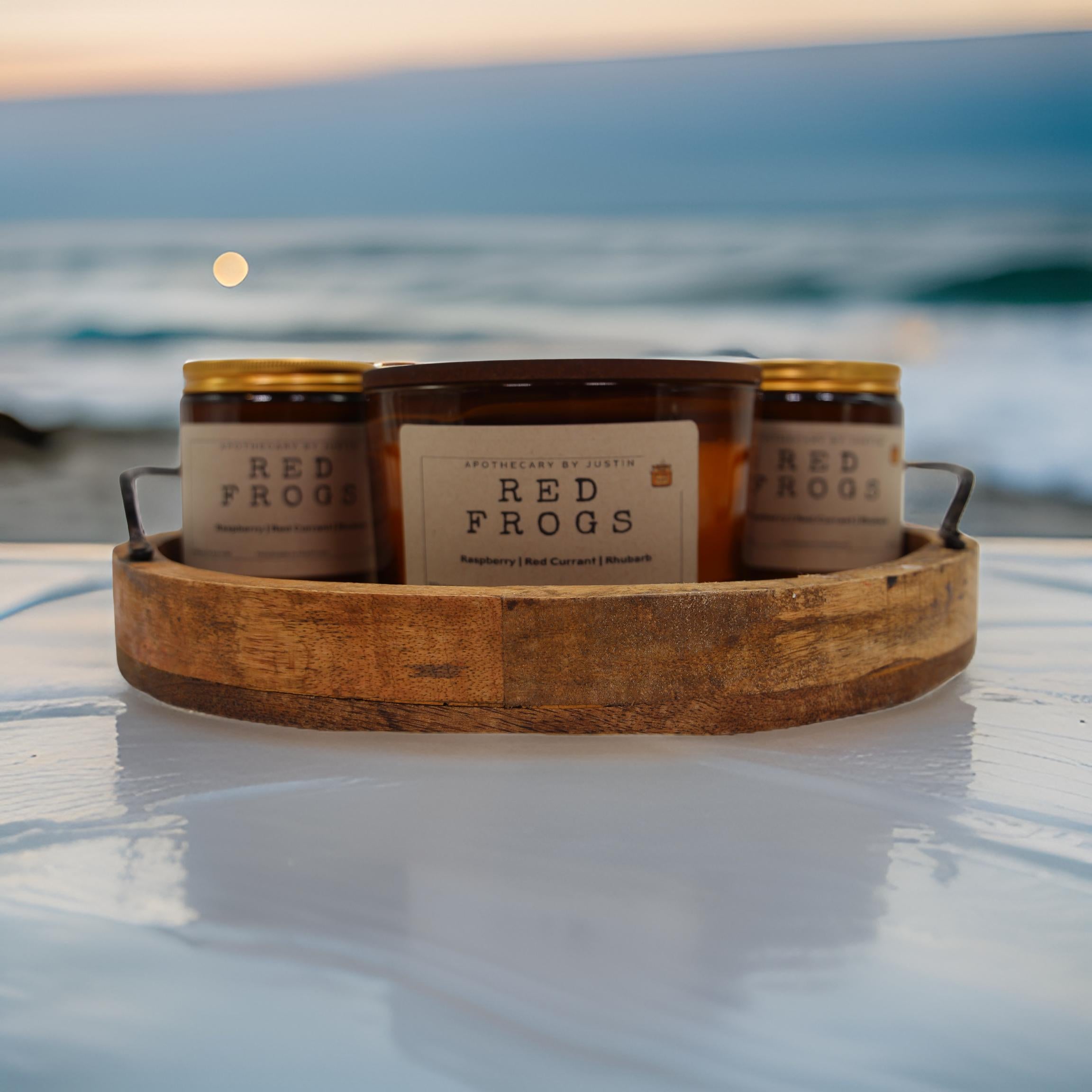 My Store vegan soy candle raspberry displayed in rustic wooden tray by the beach at sunset