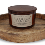 Langham Deluxe strong hot-throw woodsy candle in an amber jar with a wooden lid on a rustic wooden tray