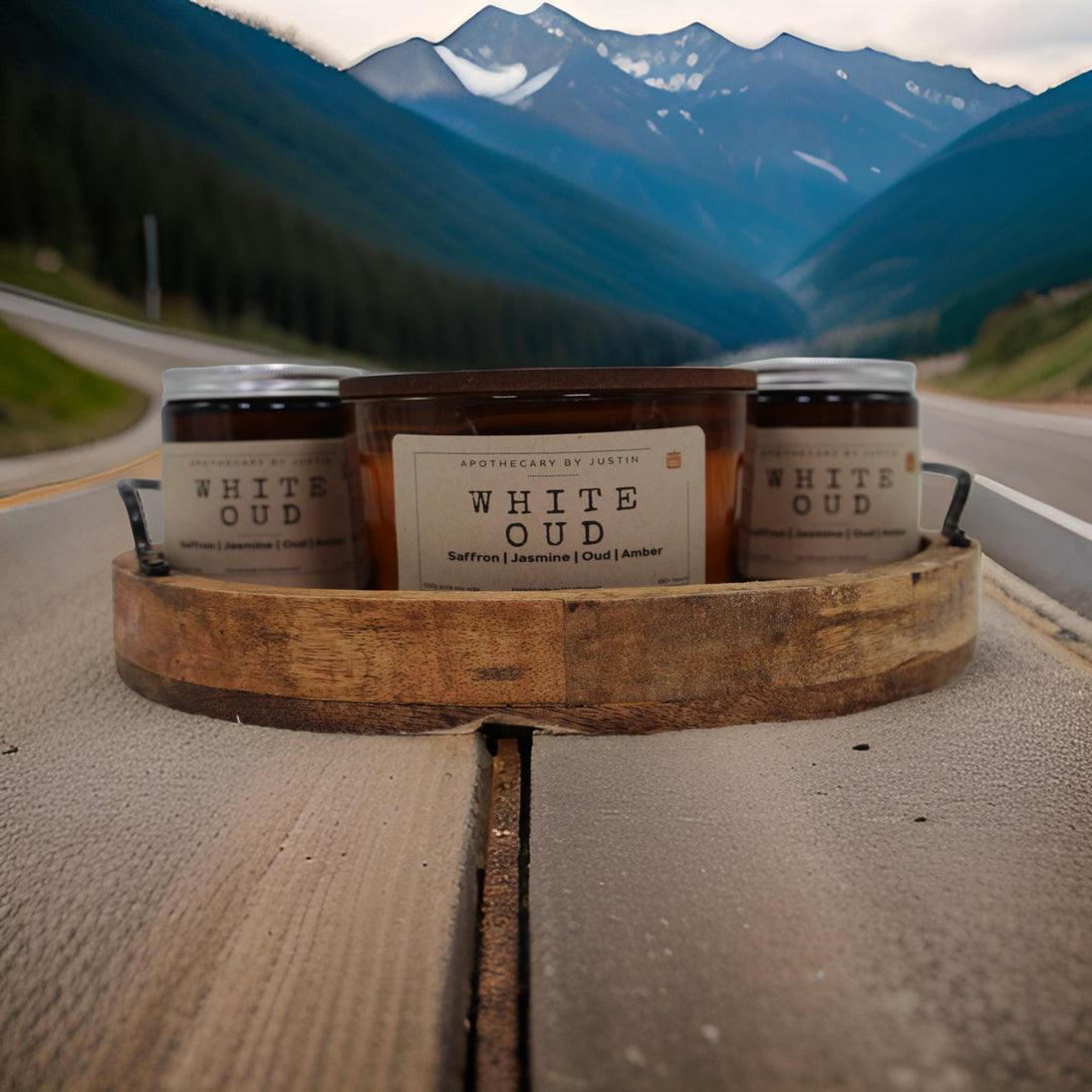 Strong hot-throw amber candle by My Store displayed on a wooden tray in a scenic mountain road setting